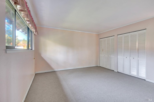 unfurnished bedroom with ornamental molding, carpet floors, and two closets