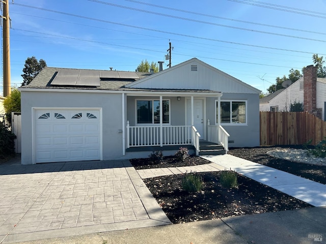 view of front facade with covered porch, solar panels, and a garage