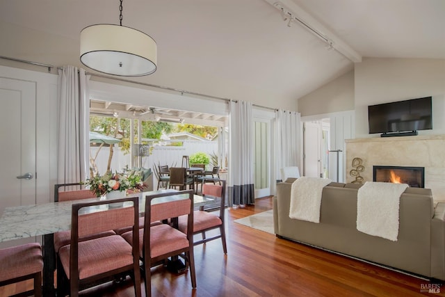 dining area featuring a high end fireplace, track lighting, vaulted ceiling with beams, and wood-type flooring