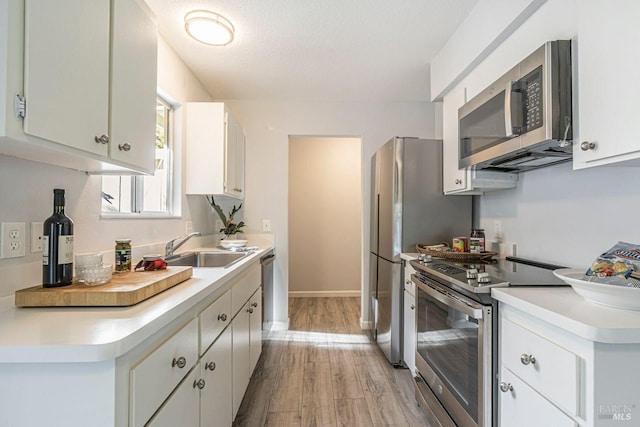 kitchen featuring sink, light wood-type flooring, a textured ceiling, appliances with stainless steel finishes, and white cabinetry