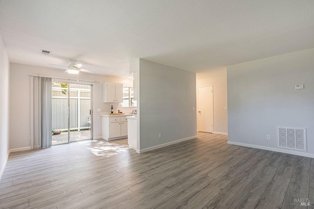 unfurnished living room with hardwood / wood-style floors, ceiling fan, and a textured ceiling