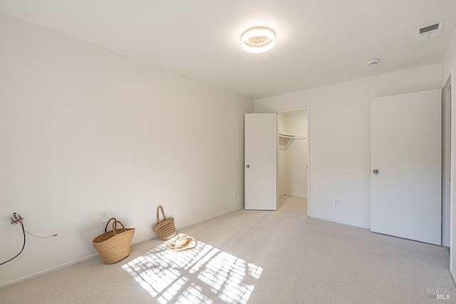 unfurnished bedroom with a spacious closet, a closet, and light carpet