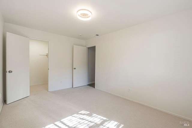 unfurnished bedroom featuring a walk in closet, light carpet, and a closet