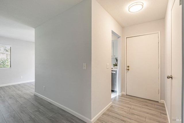 hallway with light wood-type flooring and a textured ceiling