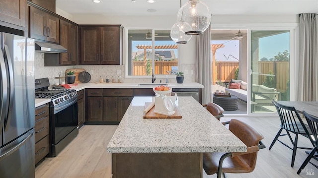 kitchen featuring stainless steel appliances, a kitchen bar, a wealth of natural light, and light wood-type flooring