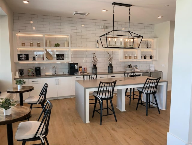 bar featuring decorative backsplash, sink, light wood-type flooring, and white cabinets