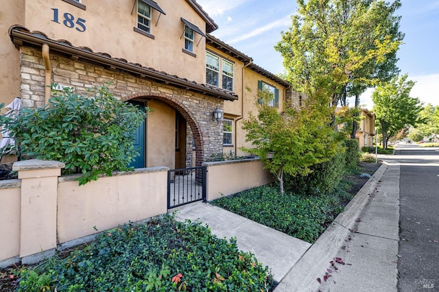 entrance to property with fence, a gate, stone siding, and stucco siding