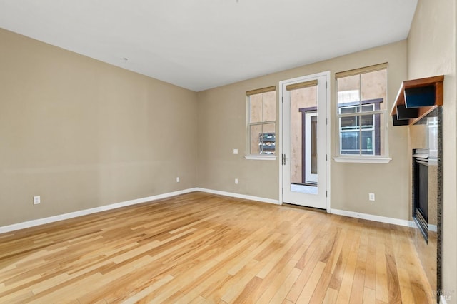 spare room featuring baseboards, a glass covered fireplace, and hardwood / wood-style floors