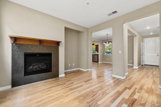 unfurnished living room with a chandelier, a glass covered fireplace, baseboards, light wood-type flooring, and visible vents