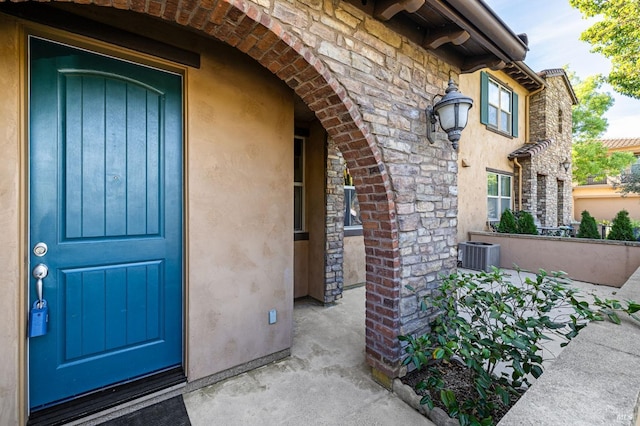 entrance to property with central AC unit, stucco siding, and stone siding