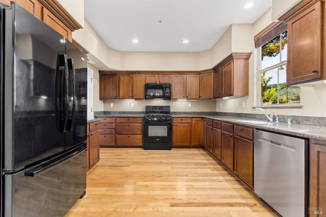 kitchen featuring dark stone countertops, black appliances, light hardwood / wood-style flooring, and sink