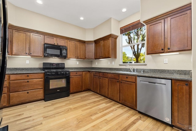 kitchen with a sink, light wood-style flooring, black appliances, and dark countertops