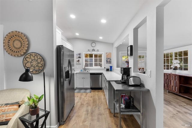 kitchen featuring lofted ceiling, light countertops, light wood-style flooring, appliances with stainless steel finishes, and a sink