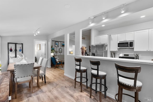 kitchen featuring white cabinets, light wood-style flooring, a breakfast bar area, stainless steel appliances, and light countertops