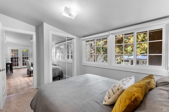 carpeted bedroom featuring french doors, a closet, vaulted ceiling, a textured ceiling, and multiple windows