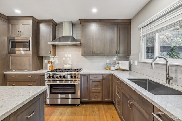 kitchen with wall chimney range hood, sink, tasteful backsplash, light stone counters, and stainless steel appliances