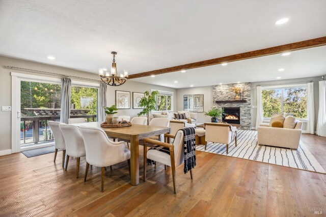 dining room with beam ceiling, a stone fireplace, a notable chandelier, and hardwood / wood-style flooring