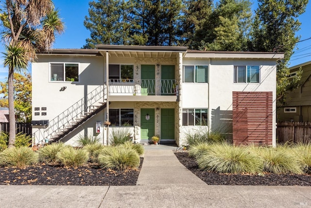 view of front facade with stairway, fence, and stucco siding