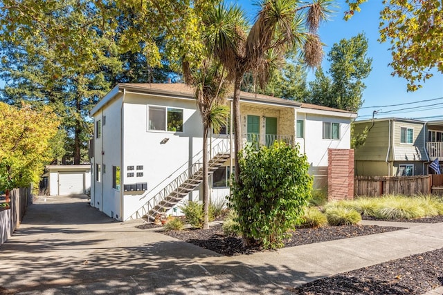 view of front of property featuring an outbuilding, stucco siding, fence, and stairs