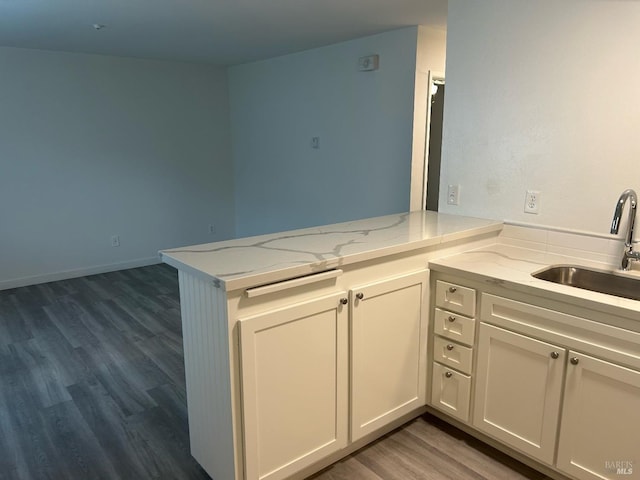 kitchen with white cabinets, light stone counters, dark wood-type flooring, a peninsula, and a sink