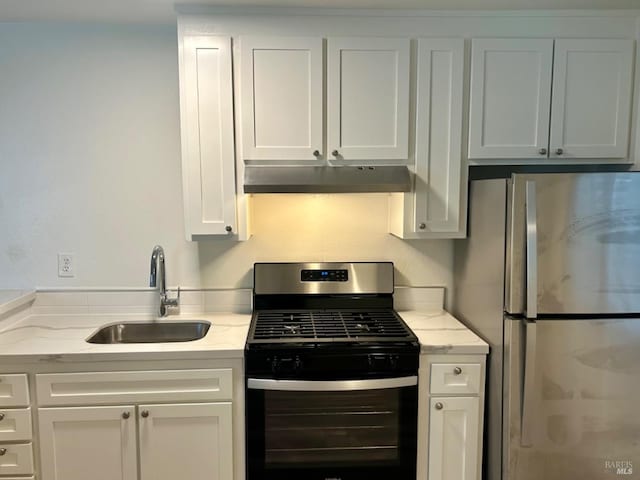 kitchen featuring appliances with stainless steel finishes, white cabinetry, a sink, light stone countertops, and under cabinet range hood