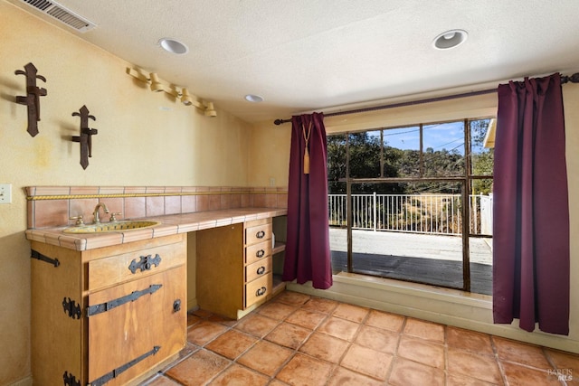 kitchen with tile countertops, sink, light tile patterned flooring, and a textured ceiling