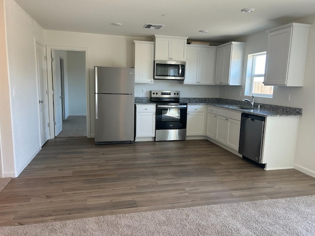 kitchen with dark hardwood / wood-style flooring, appliances with stainless steel finishes, sink, and white cabinets