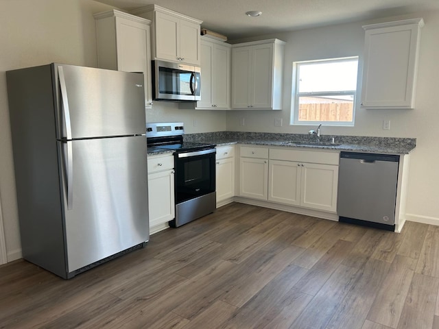 kitchen with stainless steel appliances, dark stone counters, dark hardwood / wood-style flooring, sink, and white cabinets