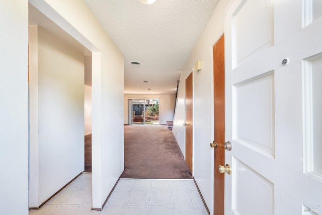 hallway with light carpet and a textured ceiling