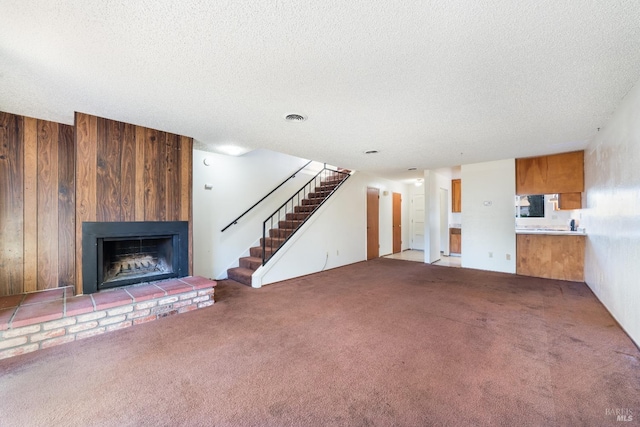 unfurnished living room with carpet flooring, wood walls, a fireplace, and a textured ceiling