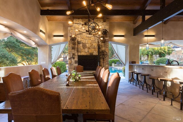 dining space with an outdoor stone fireplace, a towering ceiling, an inviting chandelier, wooden ceiling, and beamed ceiling