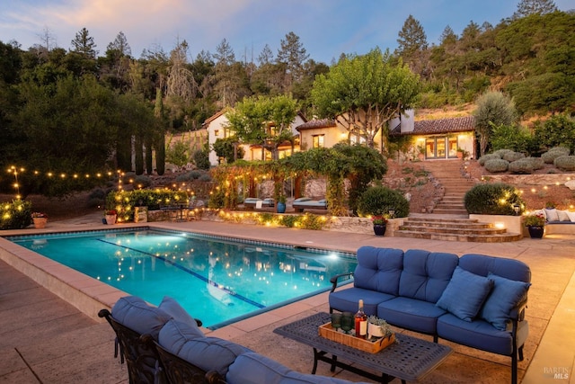 pool at dusk featuring an outdoor pool, a patio area, stairway, and an outdoor living space