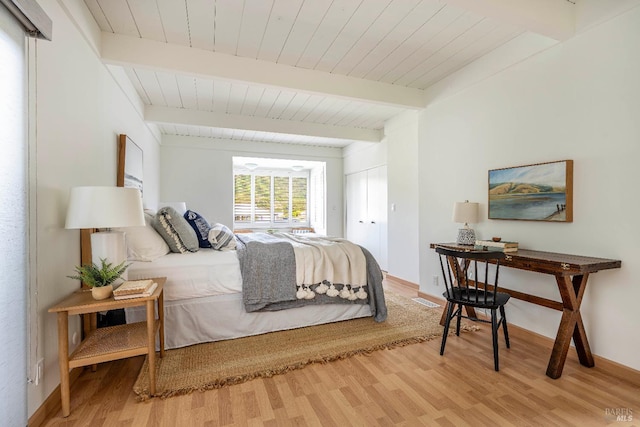 bedroom featuring baseboards, beam ceiling, wooden ceiling, light wood-style floors, and a closet