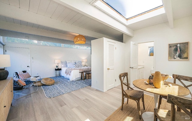 bedroom with ensuite bath, beam ceiling, and light wood-style floors