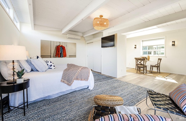 bedroom with beamed ceiling, wood ceiling, wood finished floors, a closet, and a wall mounted AC