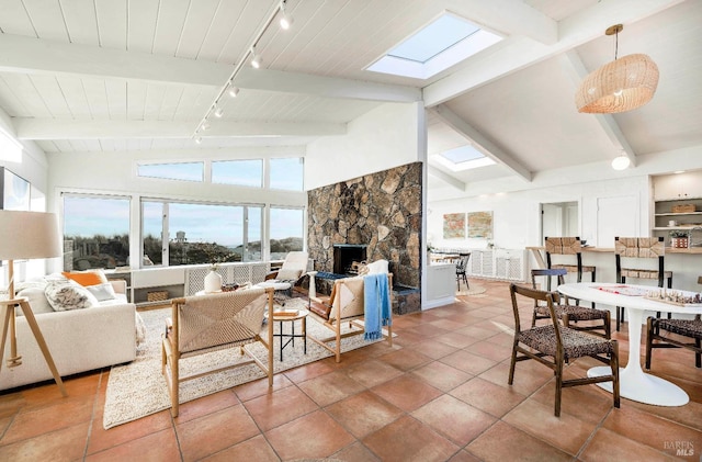 living room featuring track lighting, high vaulted ceiling, beamed ceiling, a fireplace, and a skylight