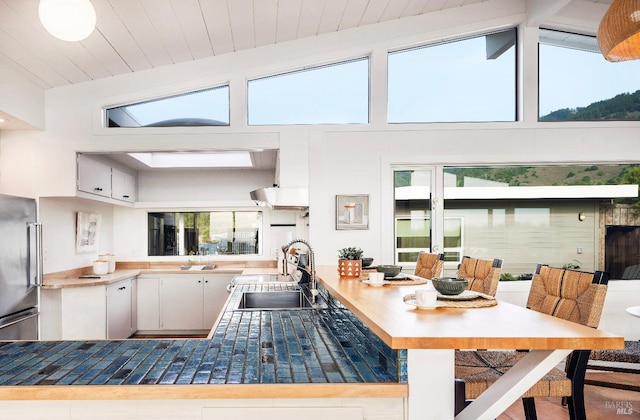 kitchen featuring sink, vaulted ceiling with beams, high quality fridge, and white cabinets