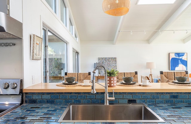 kitchen with beam ceiling, rail lighting, stainless steel stove, wooden counters, and sink