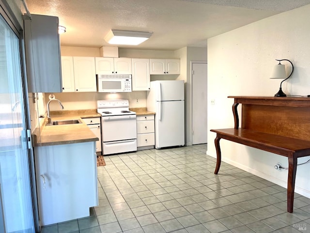 kitchen with white appliances, light tile patterned floors, a textured ceiling, white cabinetry, and sink