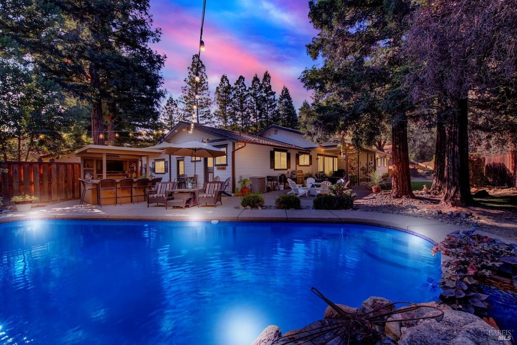 pool at dusk with a patio area, fence, a fenced in pool, and outdoor dry bar