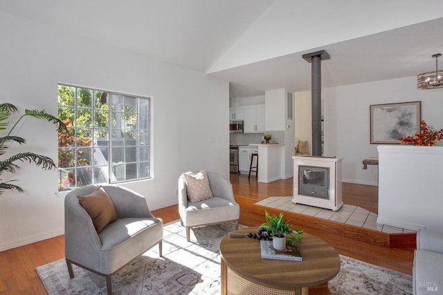 living room with a wood stove, light wood-type flooring, baseboards, and lofted ceiling