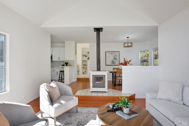 living room with light wood-style floors, a wood stove, vaulted ceiling, and baseboards