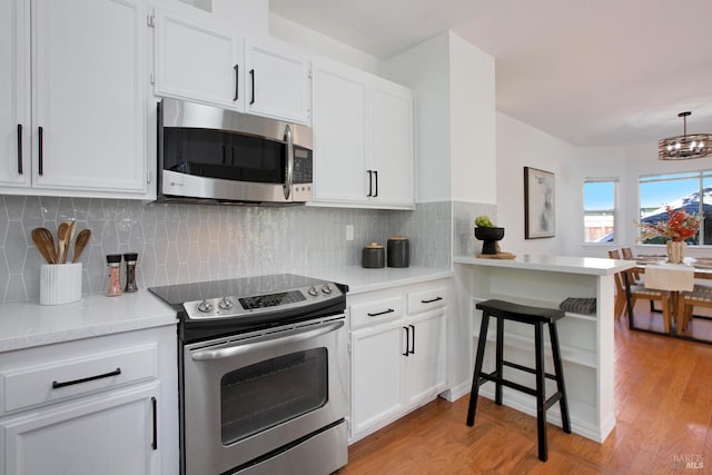 kitchen with a peninsula, light wood-style flooring, stainless steel appliances, and backsplash