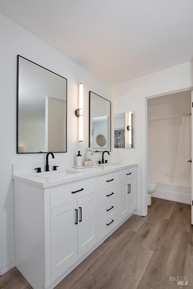 bathroom featuring double vanity, a sink, toilet, and wood finished floors