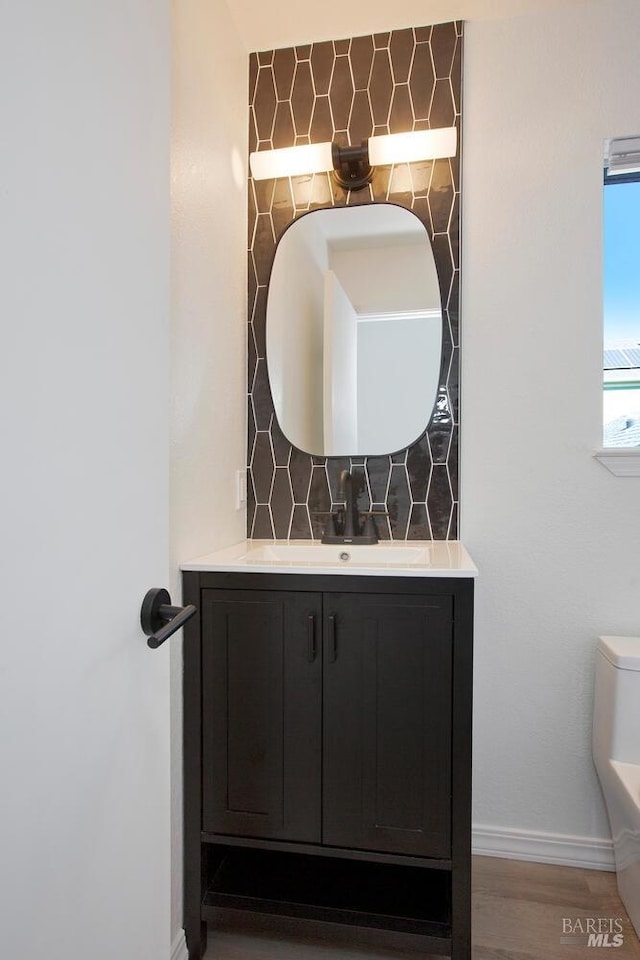 bathroom featuring baseboards, decorative backsplash, wood finished floors, and vanity