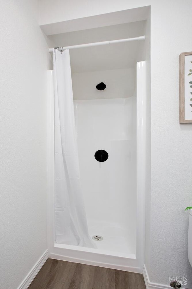 full bathroom featuring a stall shower, baseboards, and wood finished floors