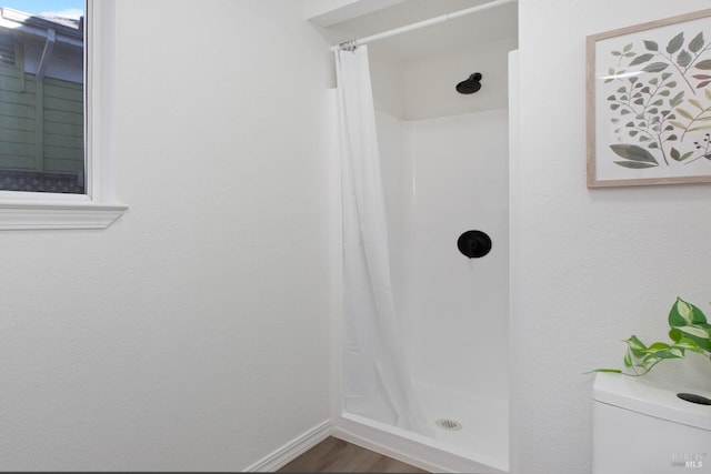 bathroom with a stall shower, baseboards, toilet, and wood finished floors