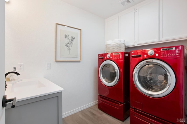 clothes washing area with light wood-style flooring, a sink, visible vents, cabinet space, and washing machine and clothes dryer