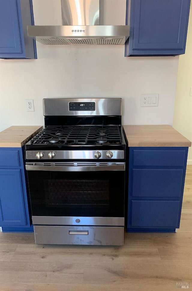 kitchen featuring wall chimney exhaust hood, stainless steel range with gas stovetop, blue cabinets, and light hardwood / wood-style floors