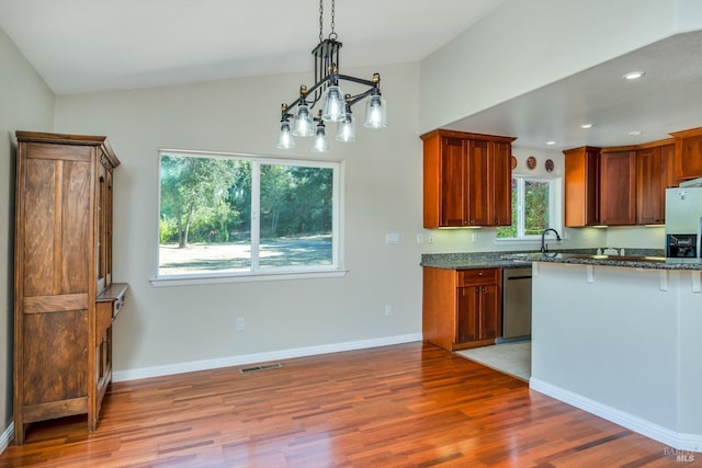 kitchen featuring lofted ceiling, dark stone counters, hanging light fixtures, stainless steel dishwasher, and light wood-type flooring